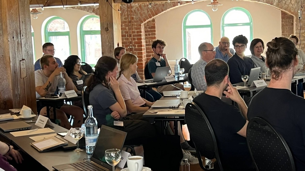 Eine Gruppe Menschen in einem Raum, die an mehreren Tischen sitzen und Computer vor sich stehen haben.