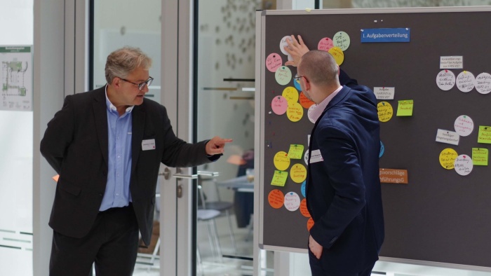 Sebastian C. Semler und Christoph Wagenblast Zwei Männer stehen vor einer Pinnwand, auf der mehrere bunte, beschriebene Zettel angepinnt sind